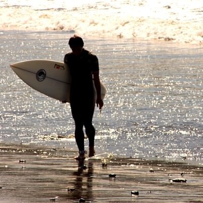 砂浜を歩くサーファーの写真