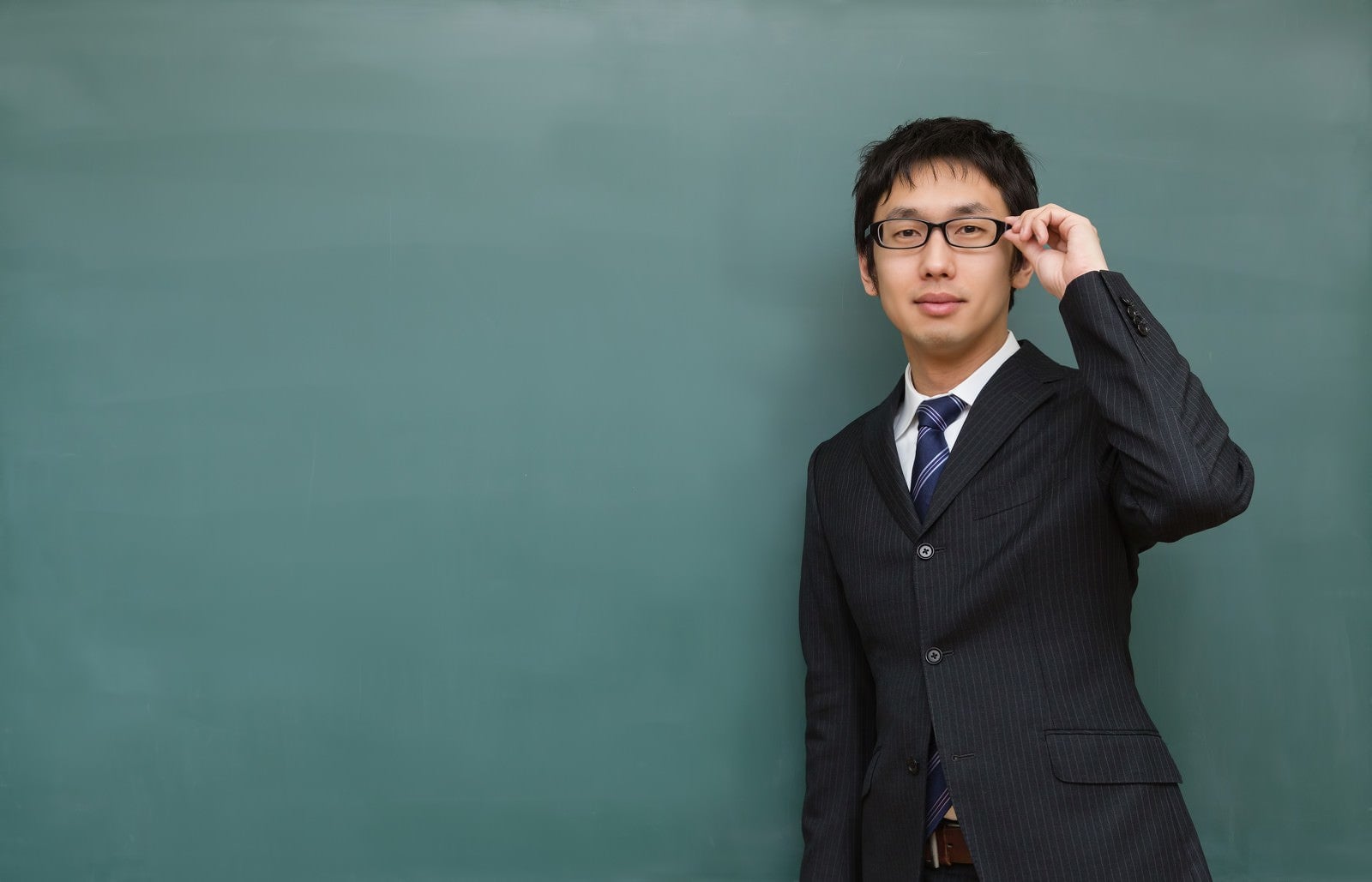 「メガネをかけた塾の講師と黒板」の写真［モデル：大川竜弥］