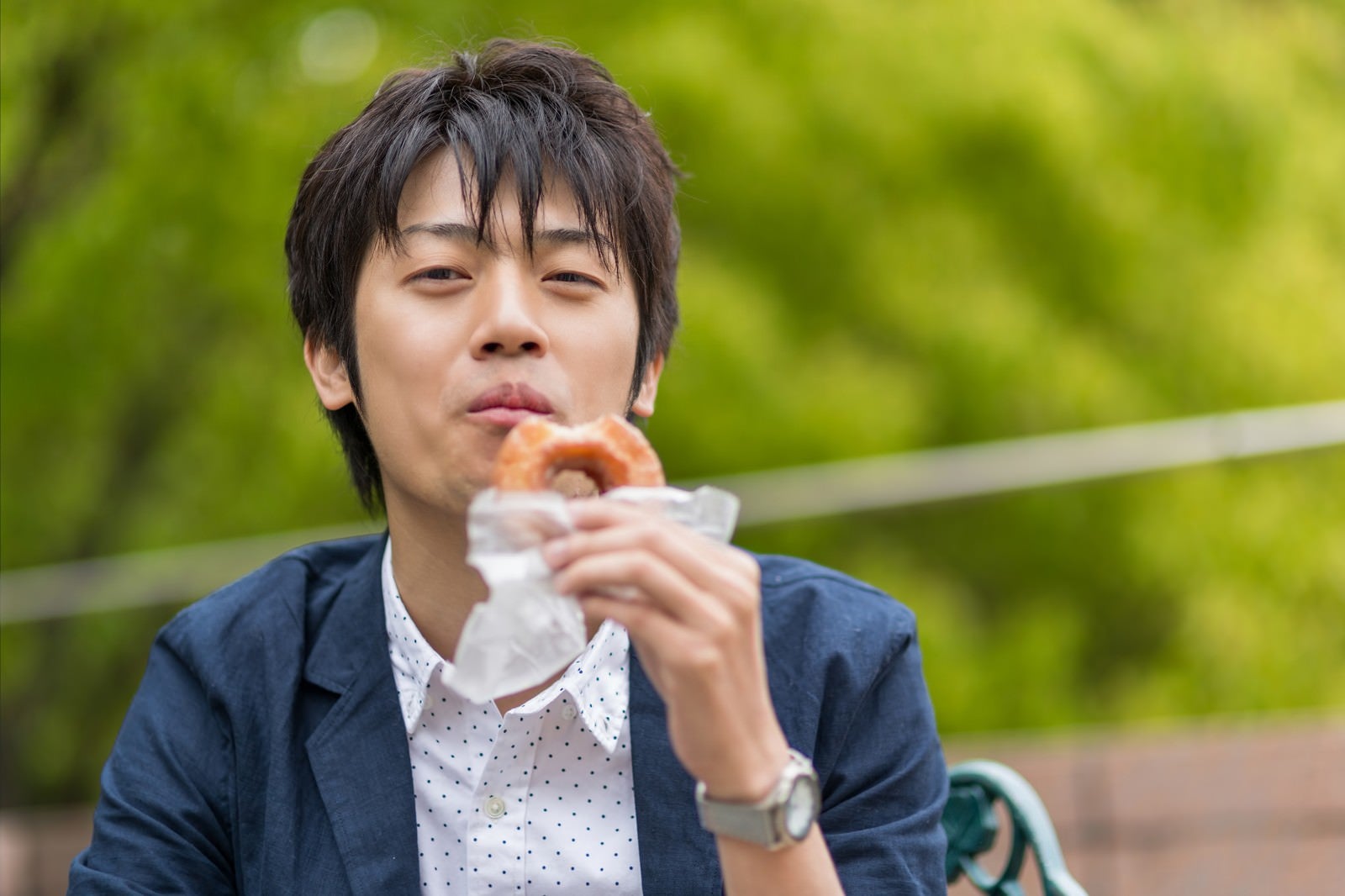 「笑顔でドーナツを食べるWebデザイナー」の写真［モデル：Tsuyoshi.］