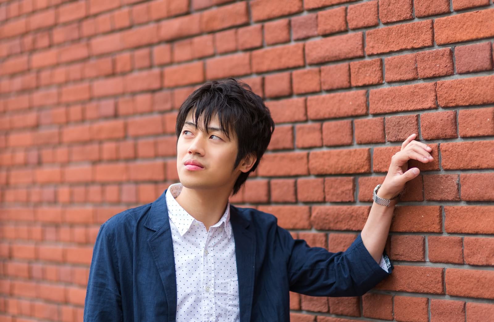 「レンガの壁に寄りかかる青年」の写真［モデル：Tsuyoshi.］