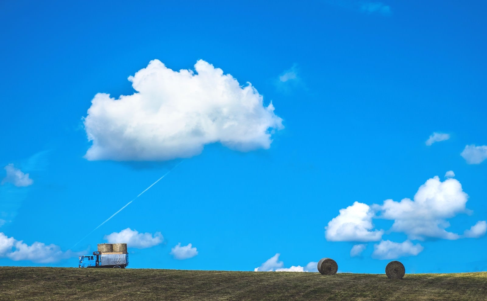 「青空の下、トラックと牧草ロール」の写真
