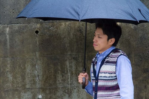 雨の日に傘を差して恋人を待つ男性の写真