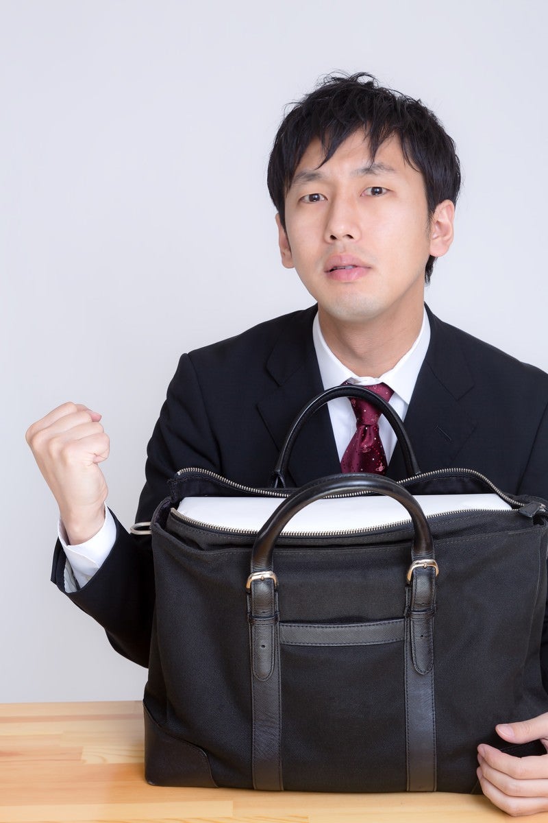 「かばんに白い箱が入ってガッツポーズを決めるビジネスマン」の写真［モデル：大川竜弥］