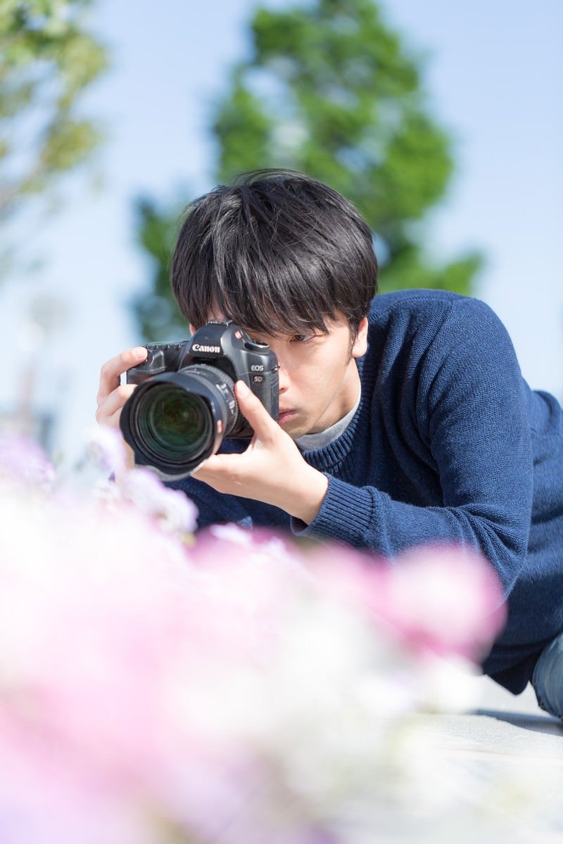 「一眼レフで花を接写するカメラマン」の写真［モデル：大川竜弥］