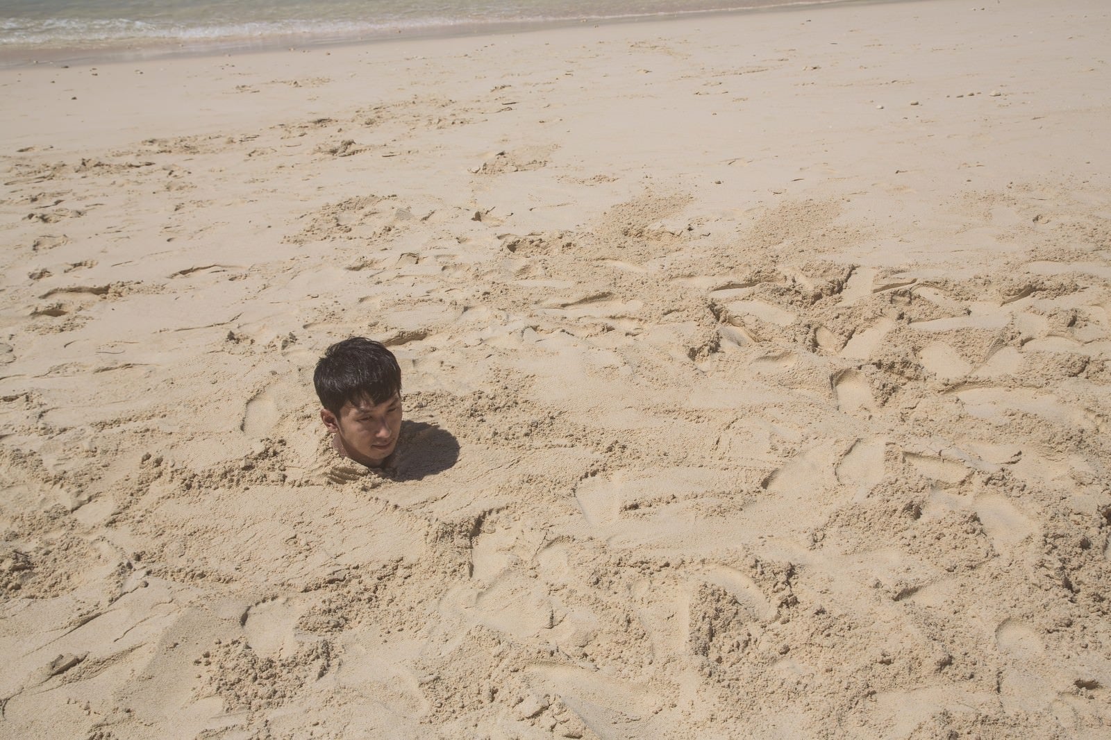 「砂浜に埋まり自身の影で方角を確認する男性」の写真［モデル：大川竜弥］