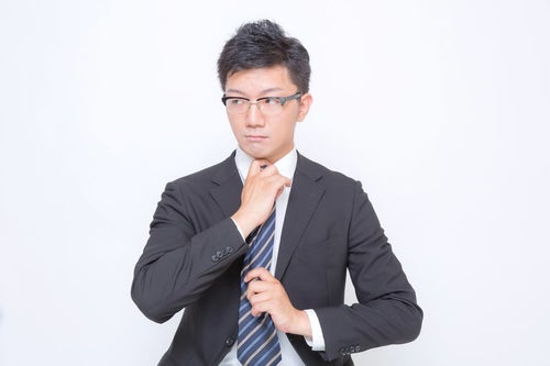 ネクタイを締め直す眼鏡をかけたビジネスマンの写真