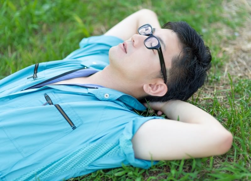 休憩中、芝生で空を眺める青い作業着姿の男性の写真