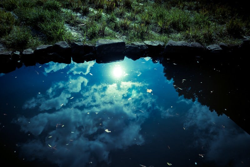 池に反射した雲と太陽の写真