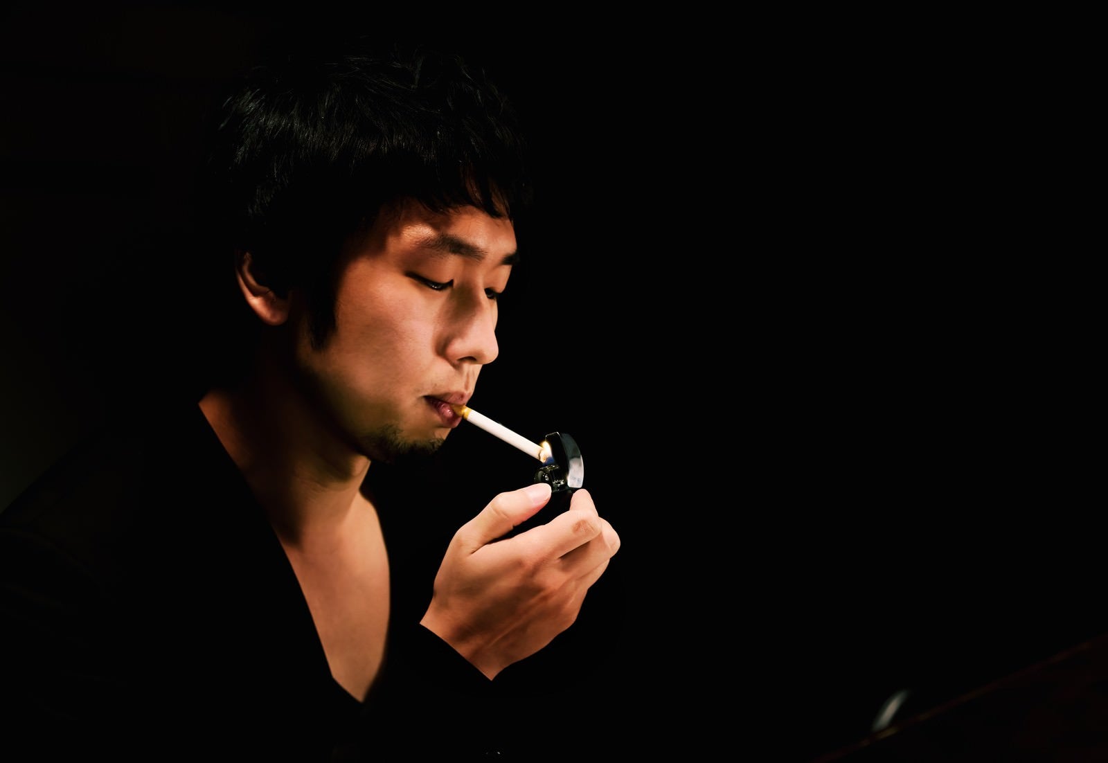 「暗いBARでタバコに火をつける男性」の写真［モデル：大川竜弥］