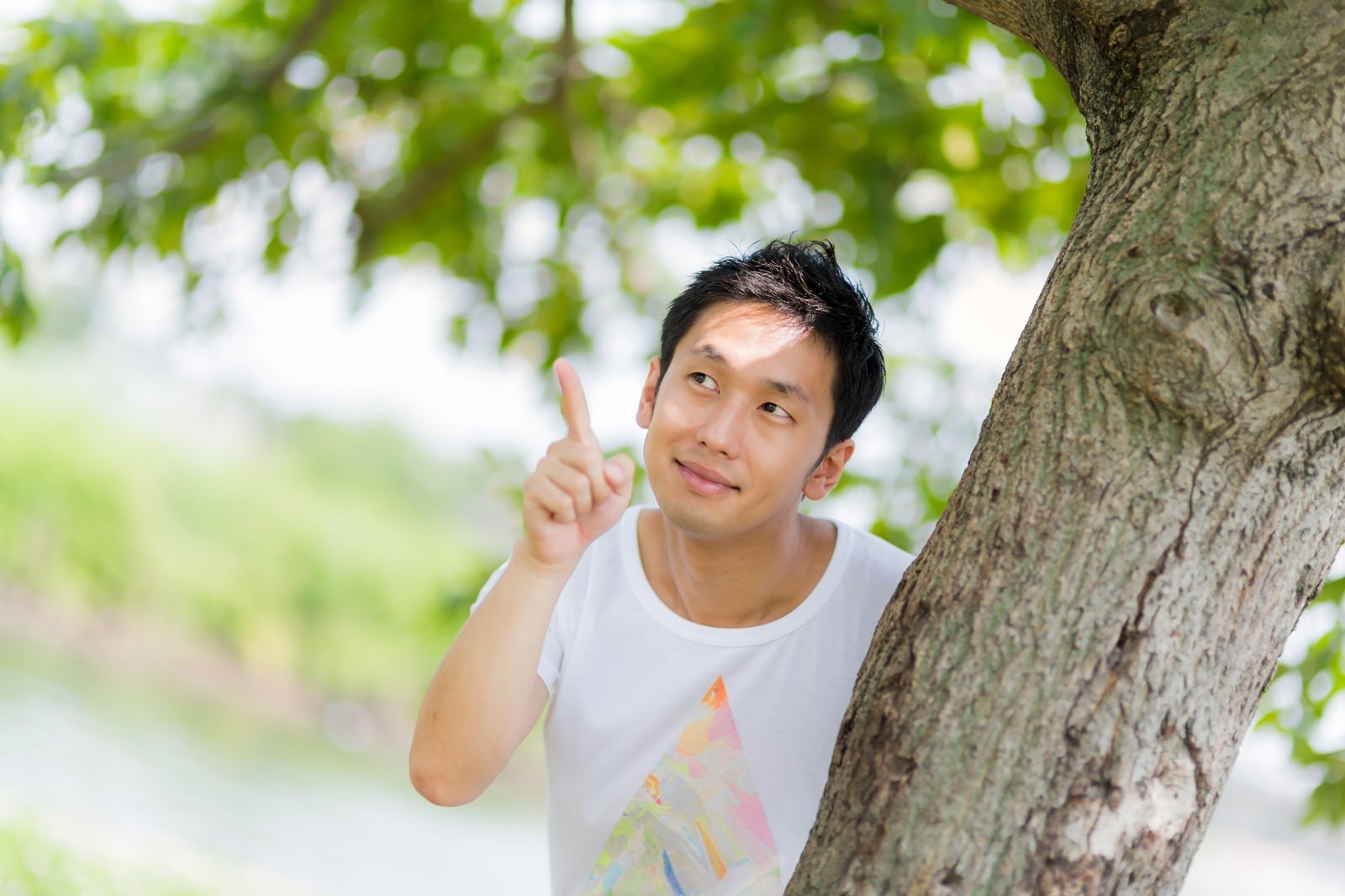 「木の陰からひょっこと現れて指をさす男性」の写真［モデル：大川竜弥］