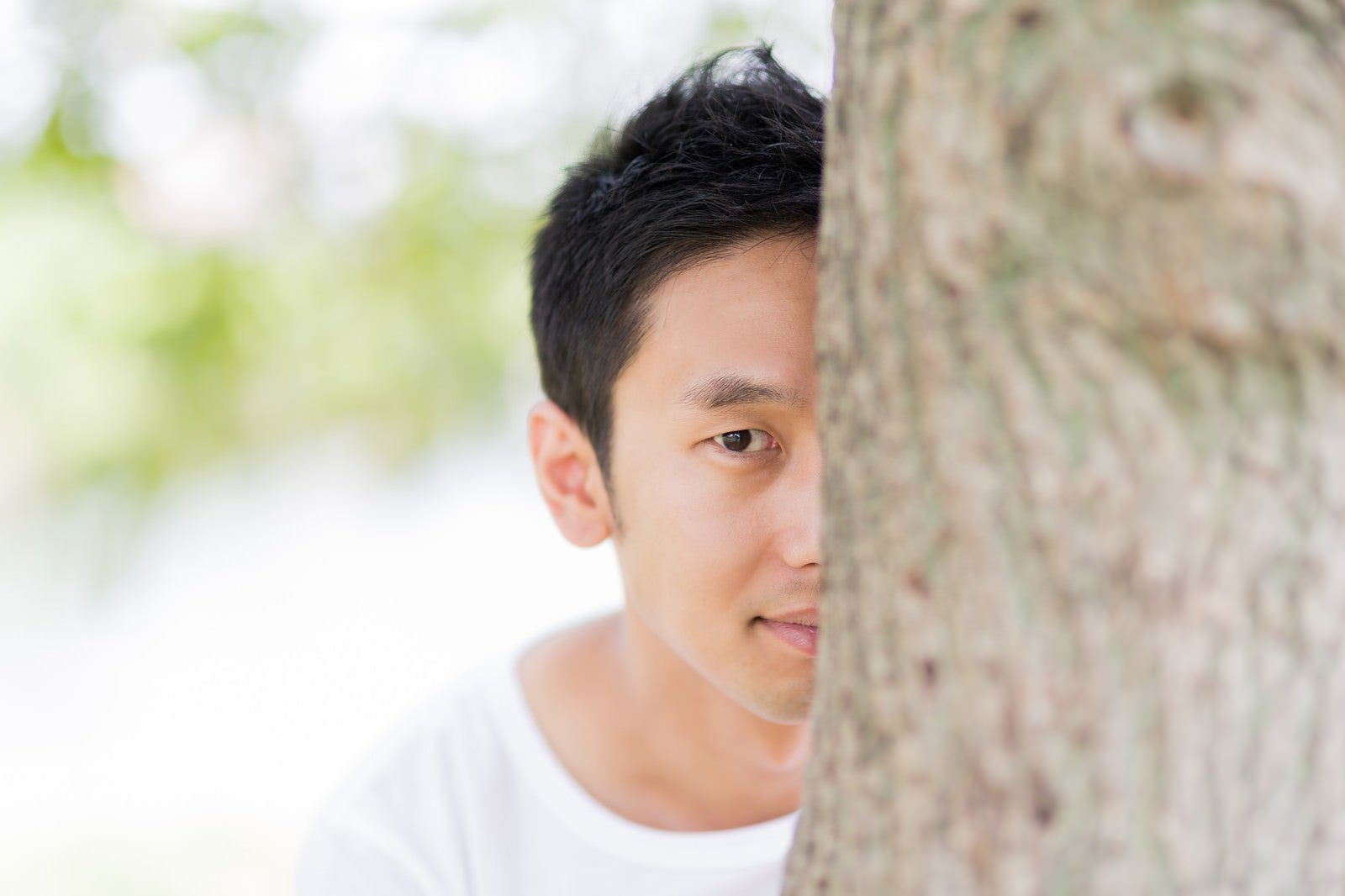 「木陰に隠れてこちらを見る男性」の写真［モデル：大川竜弥］