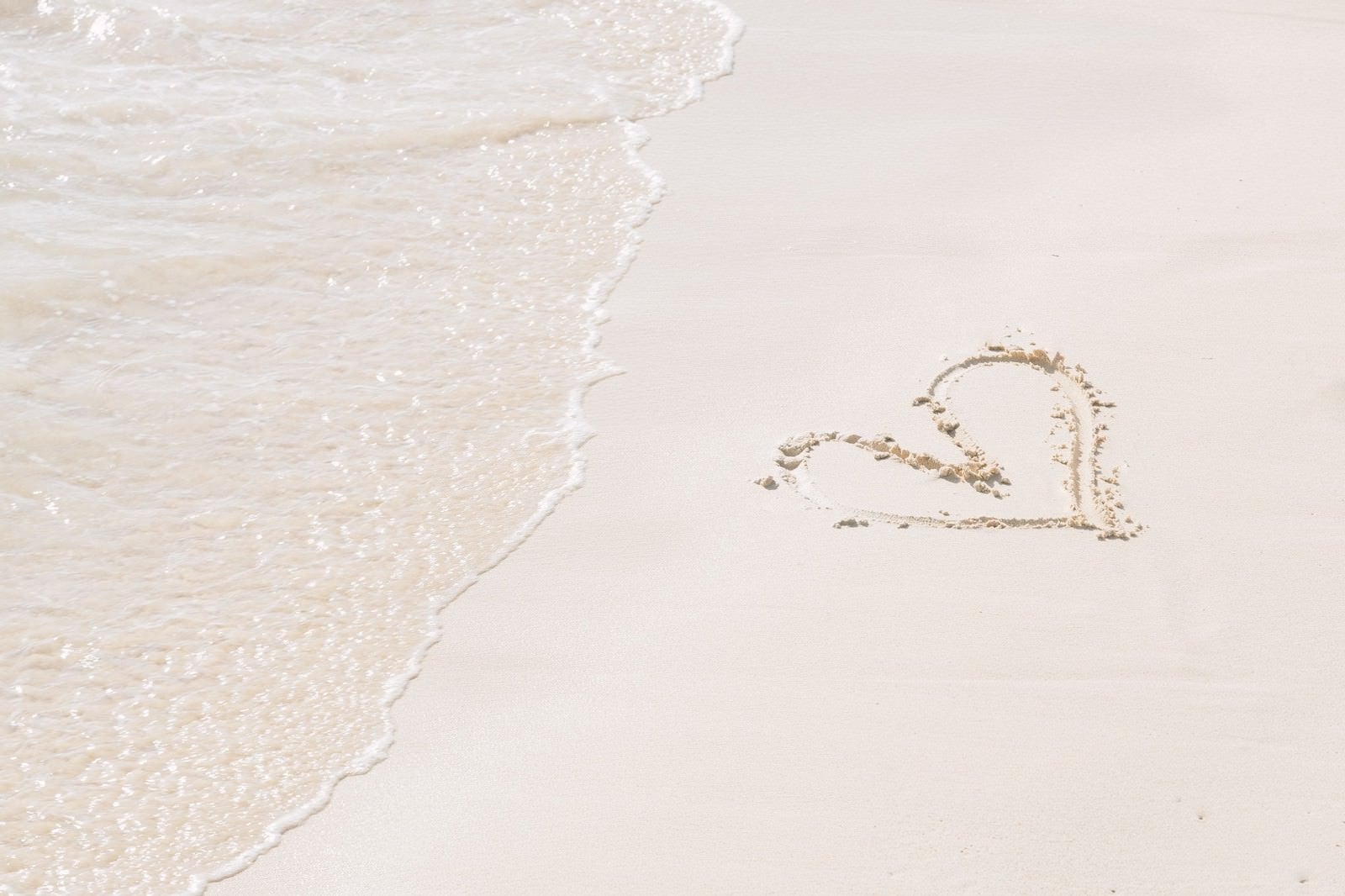 「ハートが描かれた砂浜と波」の写真