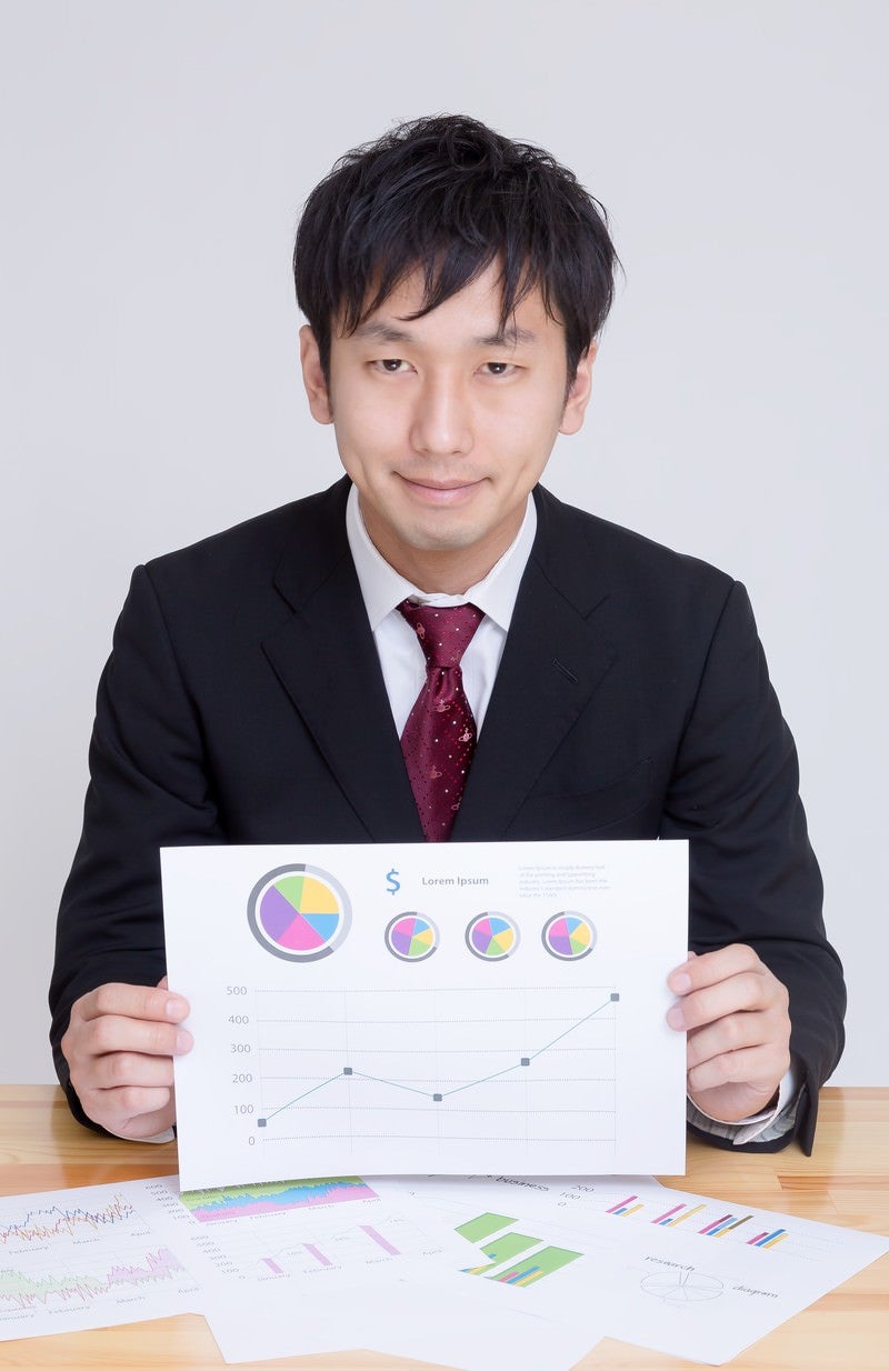 「グラフが書かれた資料を見せて提案するディレクター」の写真［モデル：大川竜弥］
