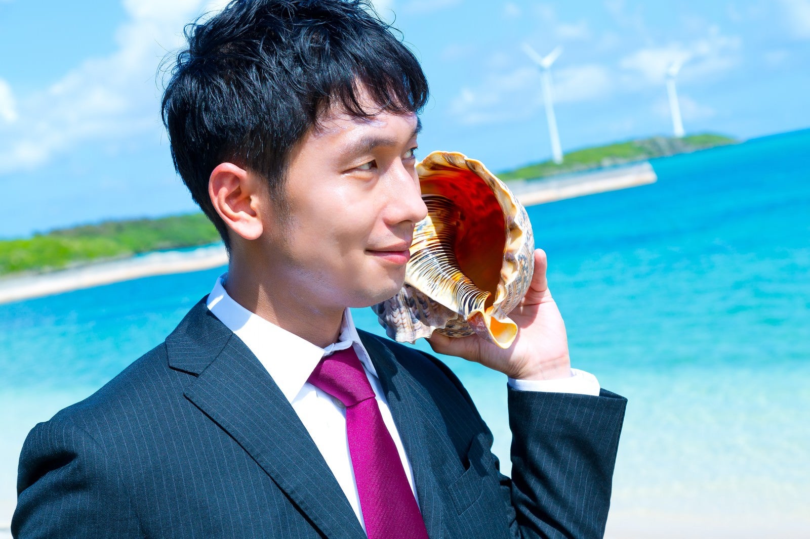 「南の島で貝フォンを使用するビジネスマン」の写真［モデル：大川竜弥］