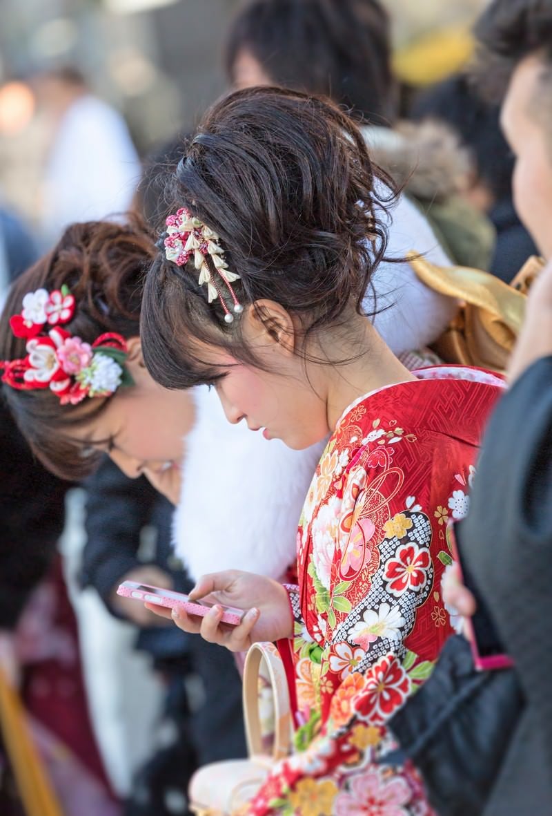 「成人式の着物姿でスマートフォンをいじる女性」の写真