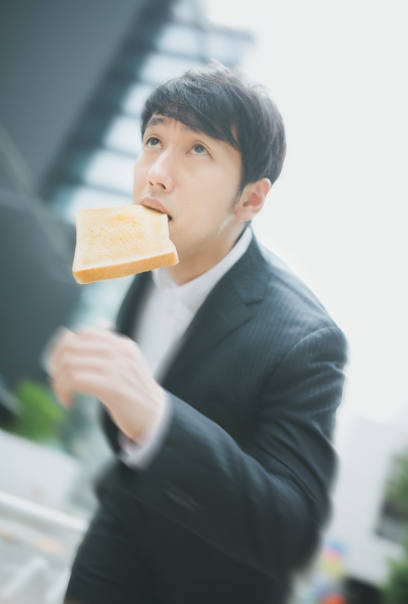 「トーストを咥え颯爽と出社するビジネスパーソン」の写真［モデル：大川竜弥］