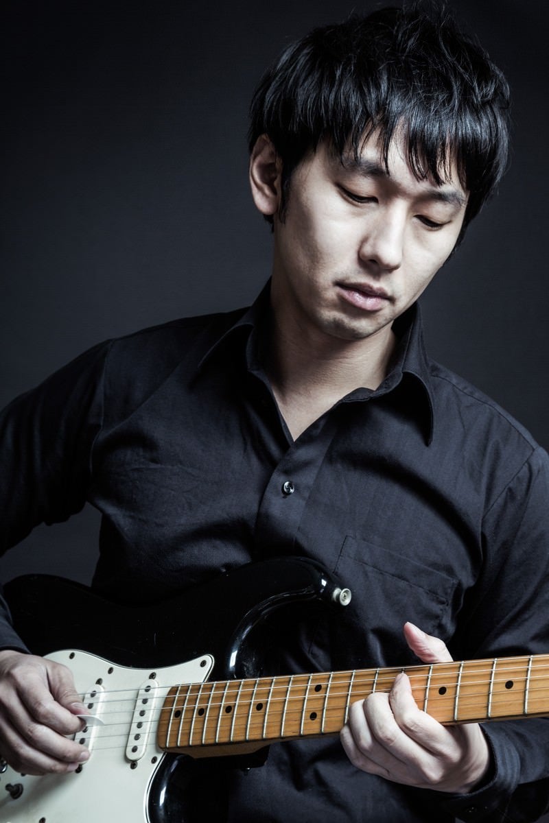 「黒いシャツと黒いギターでコーディネートするミュージシャン」の写真［モデル：大川竜弥］