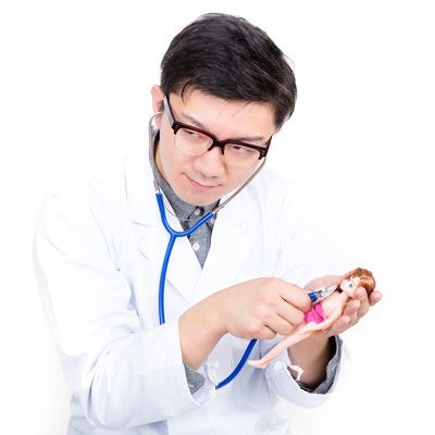 人形に聴診器を当ててお医者さんごっこをする男性の写真