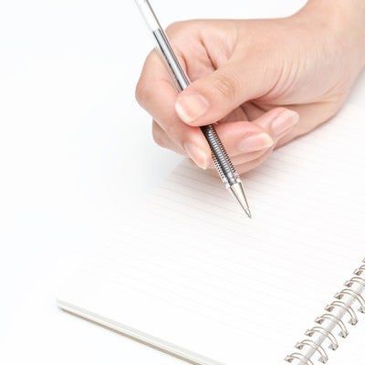 ペンを握る手とノートの写真
