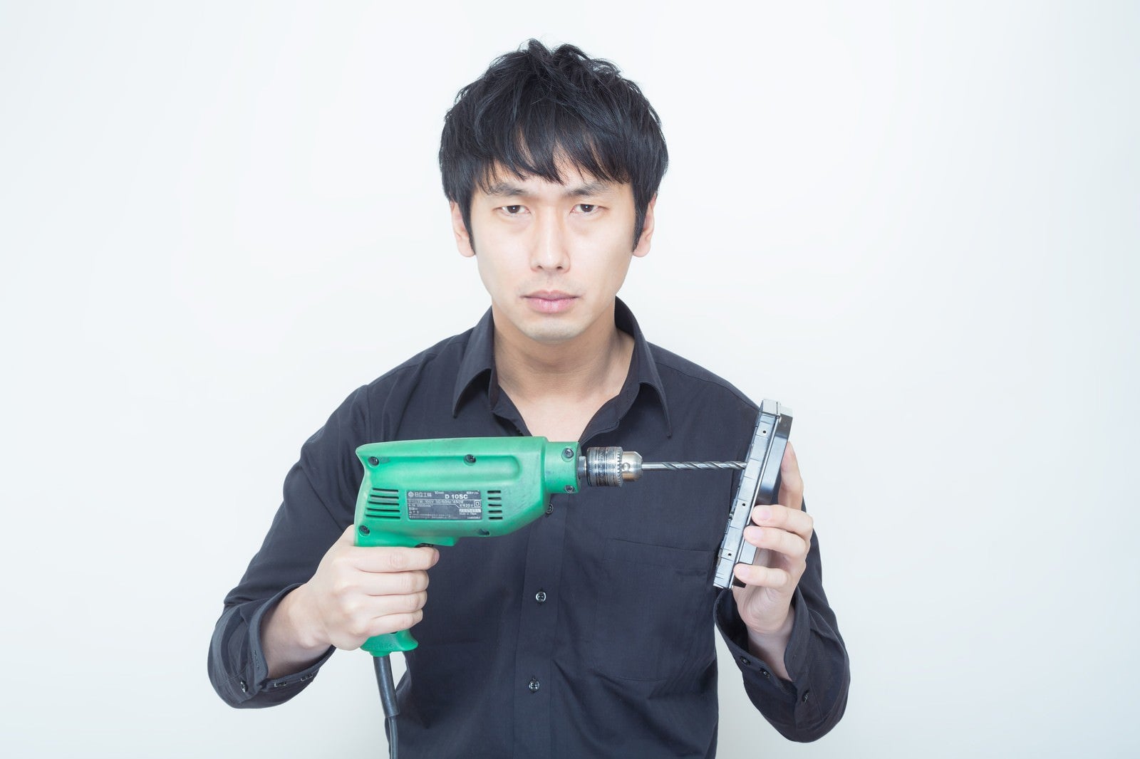 「工業用電気ドリルを使ってHDDに穴を空けようとする男性」の写真［モデル：大川竜弥］