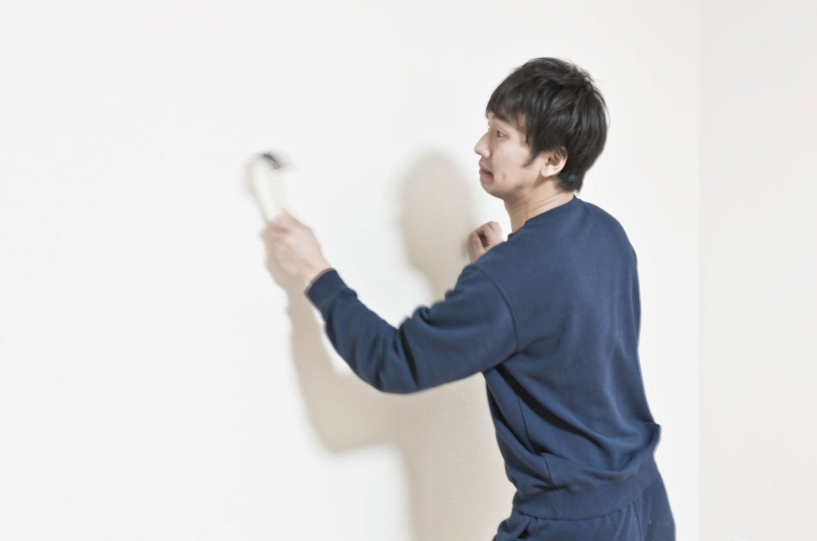 「ハンマーで壁を連打するスウェット姿の男性」の写真［モデル：大川竜弥］