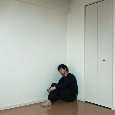 部屋の隅っこで独り寂しく寝落ちする男性の写真