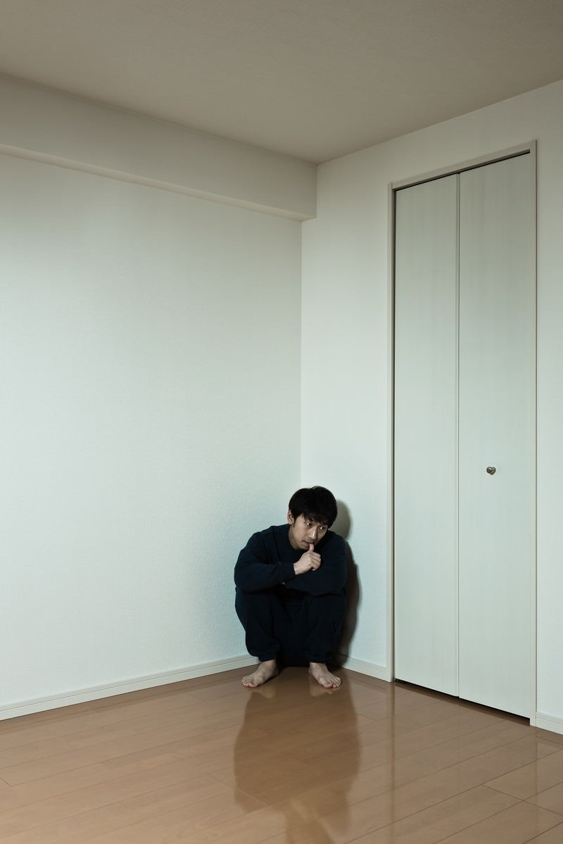 「部屋の隅っこに縮こまるスウェット姿の男性」の写真［モデル：大川竜弥］