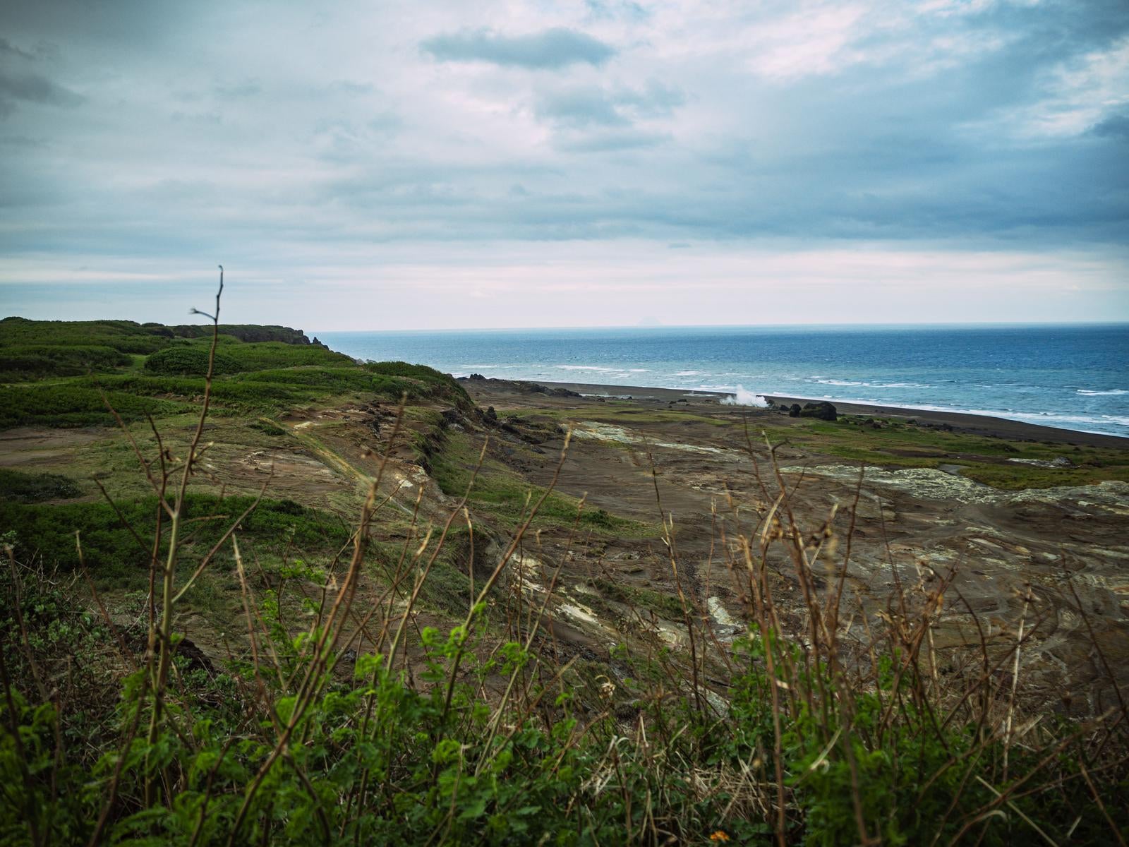 「遠景の北硫黄島と荒涼たる大地と青い海」の写真