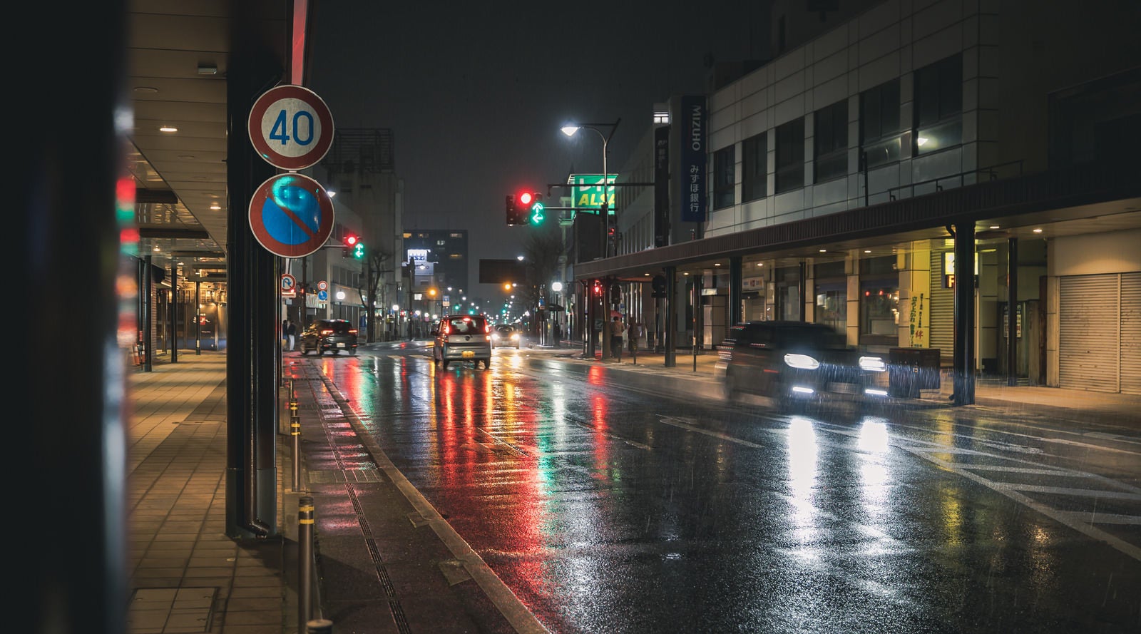 「信号と車のライトがカラフルに反射する雨の道路」の写真