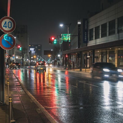 信号と車のライトがカラフルに反射する雨の道路の写真