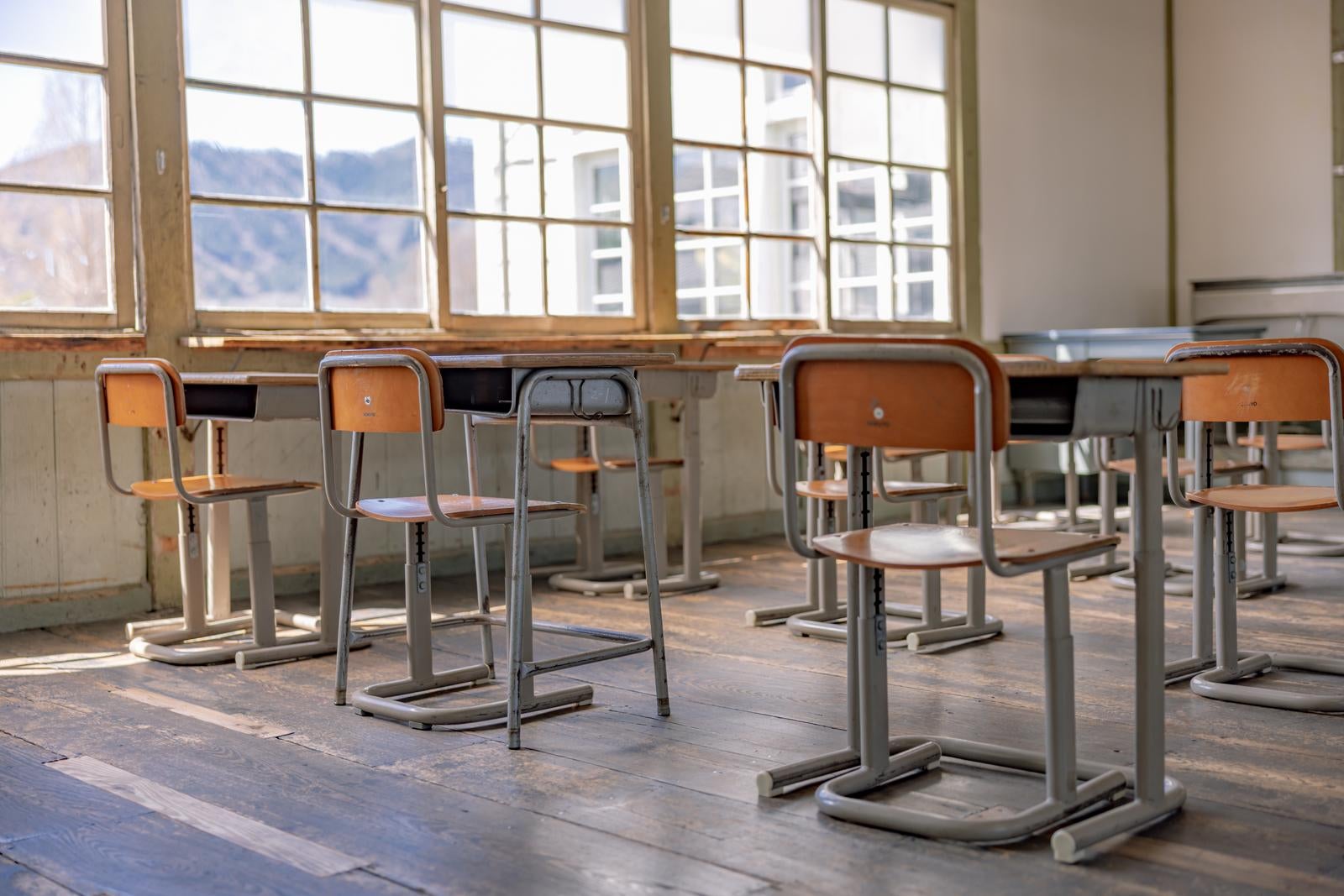 「窓から差し込む光と学習机と椅子で満たされた教室」の写真