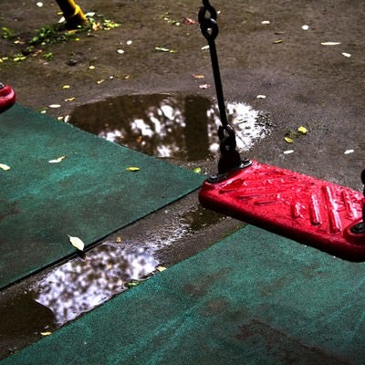 雨に濡れた赤いブランコの写真