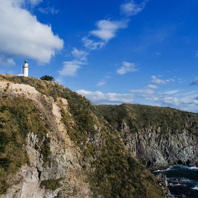 神津島の青空に映える断崖の白い灯台と荒波の写真