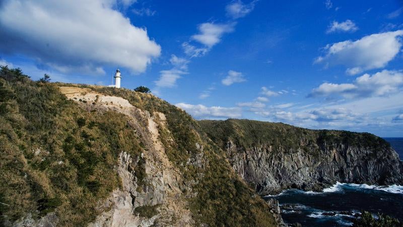 神津島の青空に映える断崖の白い灯台と荒波の写真