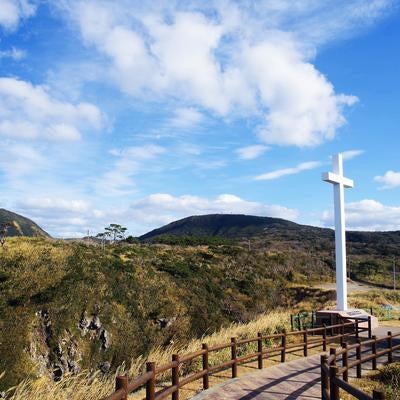 丘の上に立つ白い十字架と自然豊かな山々の写真