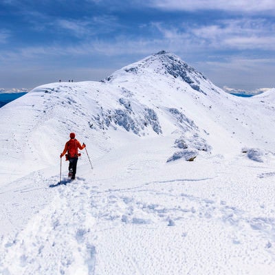 冬の乗鞍岳を登る赤い登山者の写真
