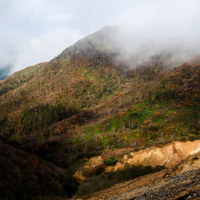雲の隙間から紅葉をのぞかせる那須岳（なすだけ）の写真