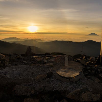 朝日に照らされる赤石岳山頂碑（南アルプス）の写真