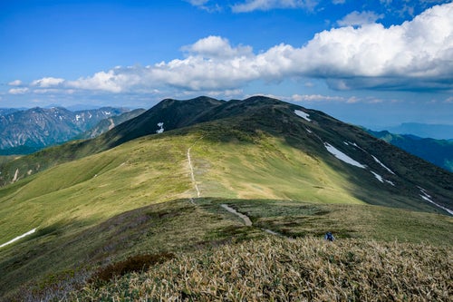 晴れ間に照らされる仙ノ倉山の稜線と登山道の写真