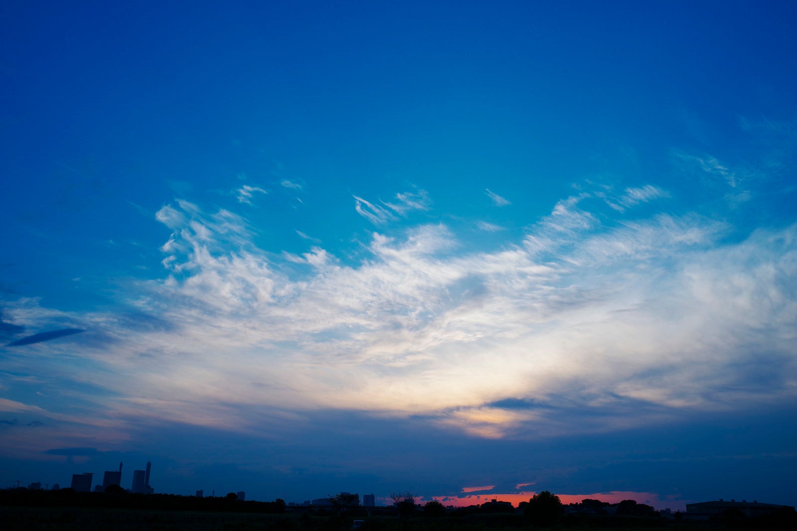 「さいたま新都心の向こうへと沈んでいく夕日と雲の青空」の写真