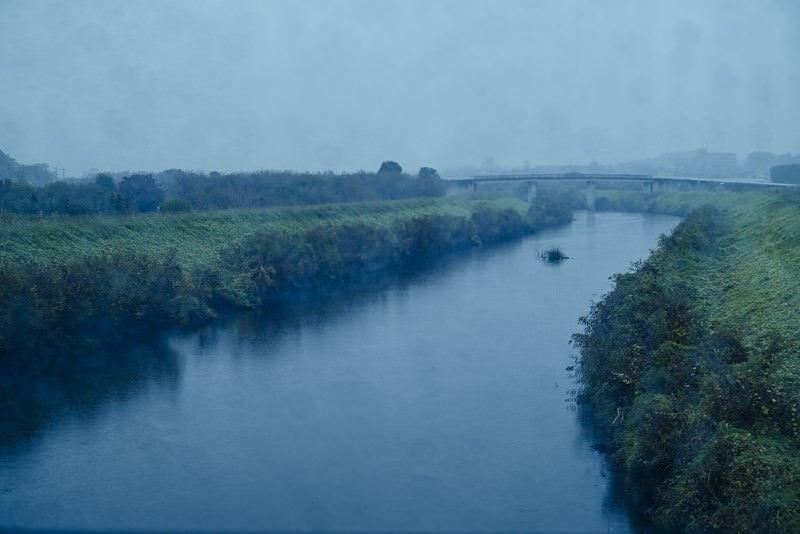 雨が降り注ぐ小川と河川敷の写真