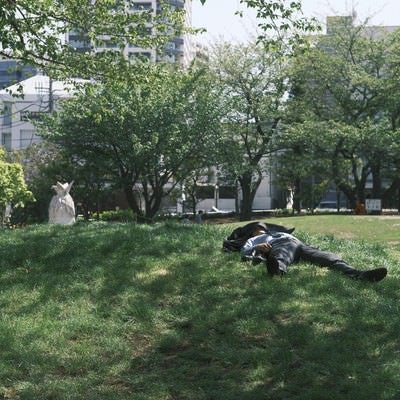 昼下がりの公園で寝る会社員の写真