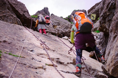 鎖が付けられた絶壁を登る登山者たちの写真