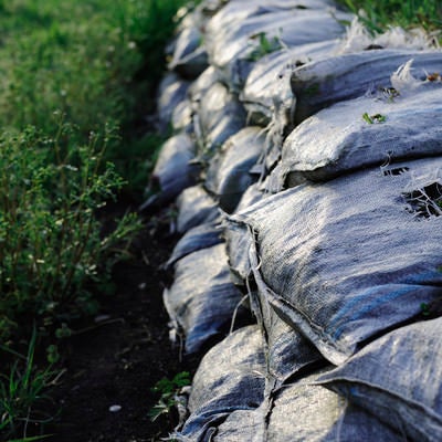 草が生えた積み上げられた砂袋と防水シートの写真