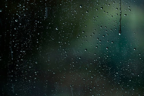 車窓に降り注ぐ雨と水滴の写真