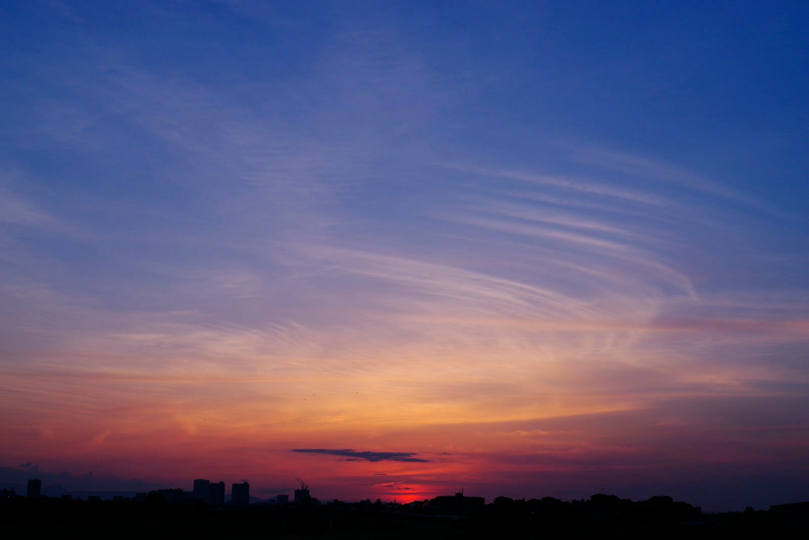 「薄い幕が重なるような空と夕日」の写真