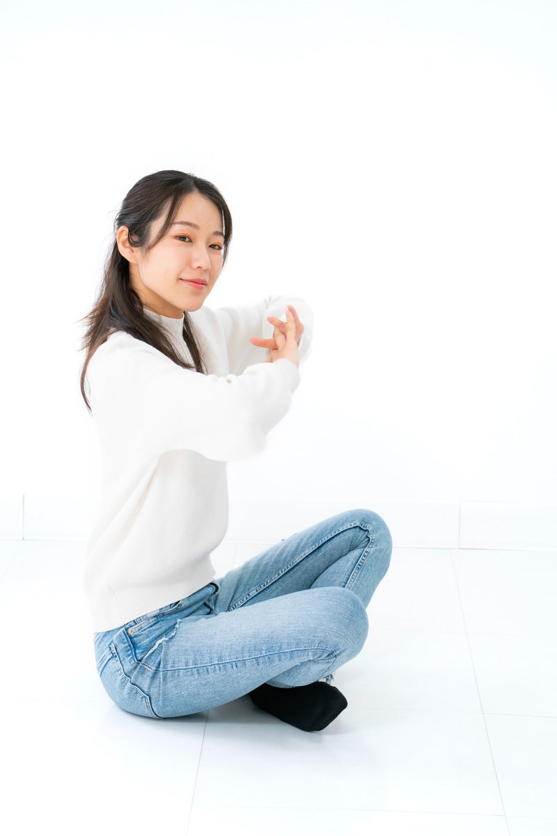「腰を下ろして伸びをしようとする女性」の写真［モデル：SAKI］