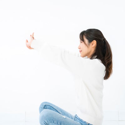 あぐら座りで腕を伸ばす女性の写真