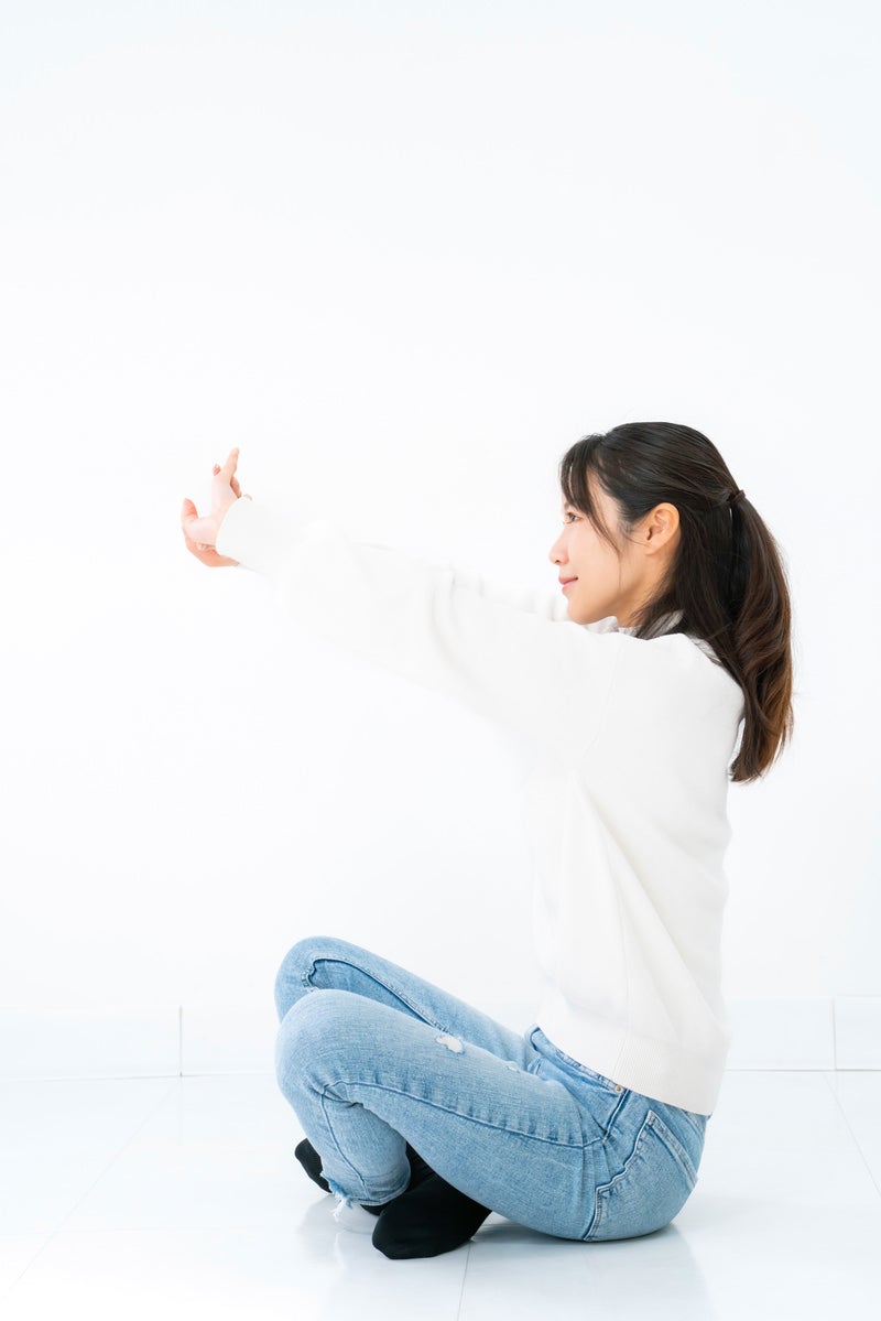 あぐら座りで腕を伸ばす女性の写真
