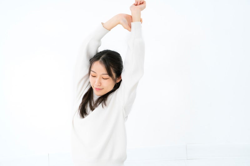 白背景で手を上に伸ばしてストレッチする女性の写真